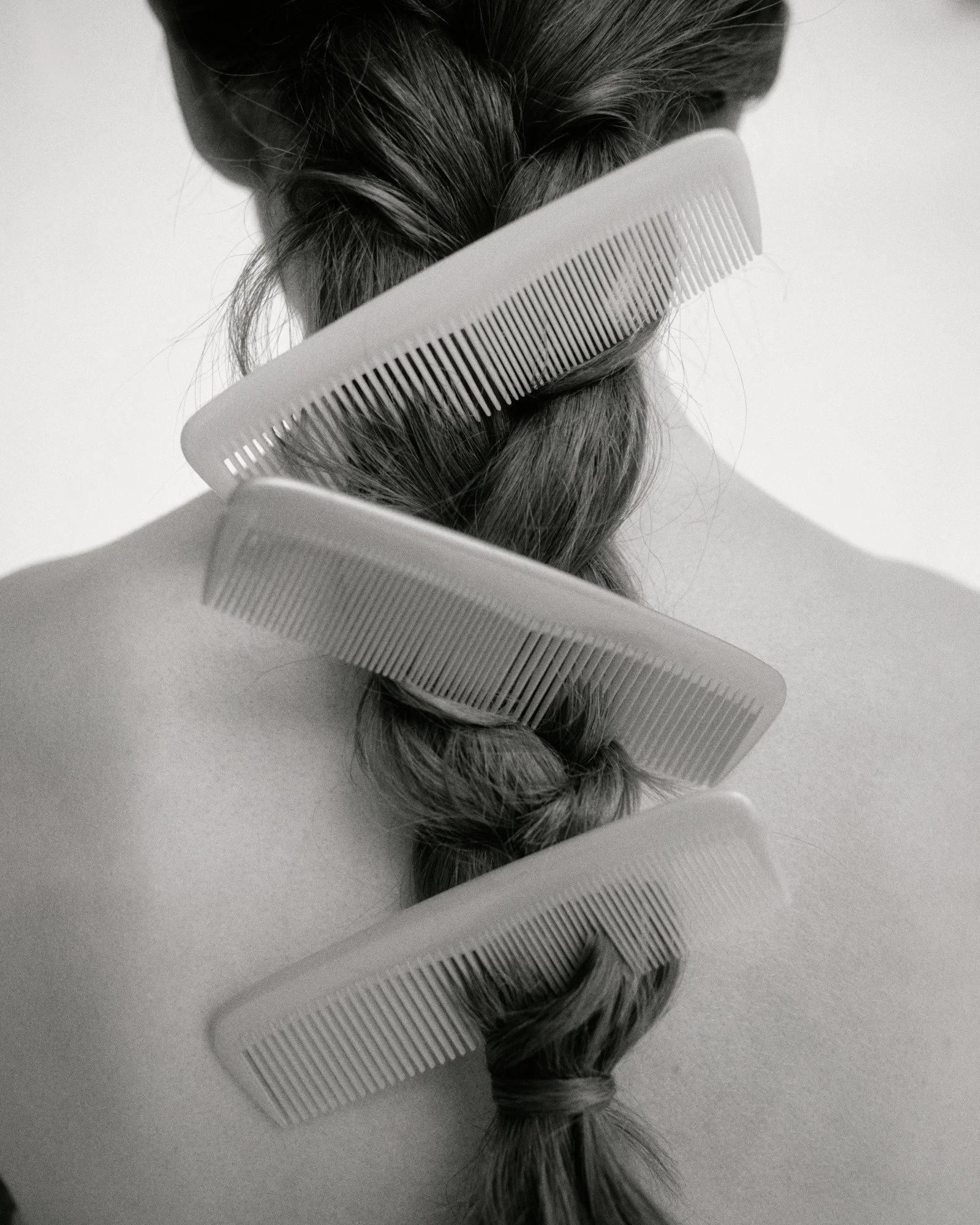 Black and white photo of a person's hair styled in a loose braid with several hair clips securing the braid, viewed from behind.