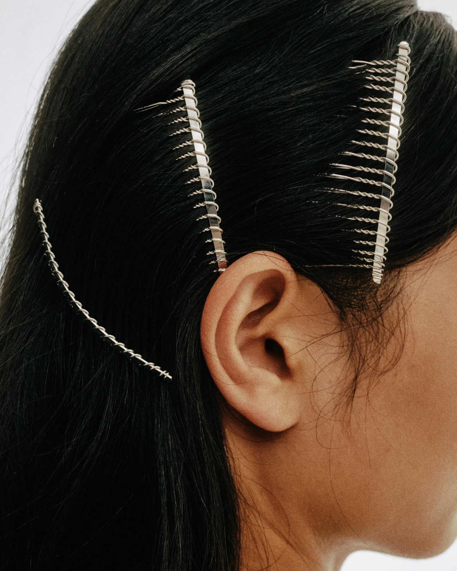 Close-up of a person with long black hair wearing hair clips and a chain accessory around the head, featuring two silver hair clips with twisted ends.