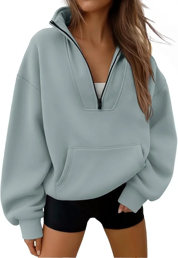 A woman wearing a light gray quarter-zip fleece pullover with a front pocket, paired with black shorts.