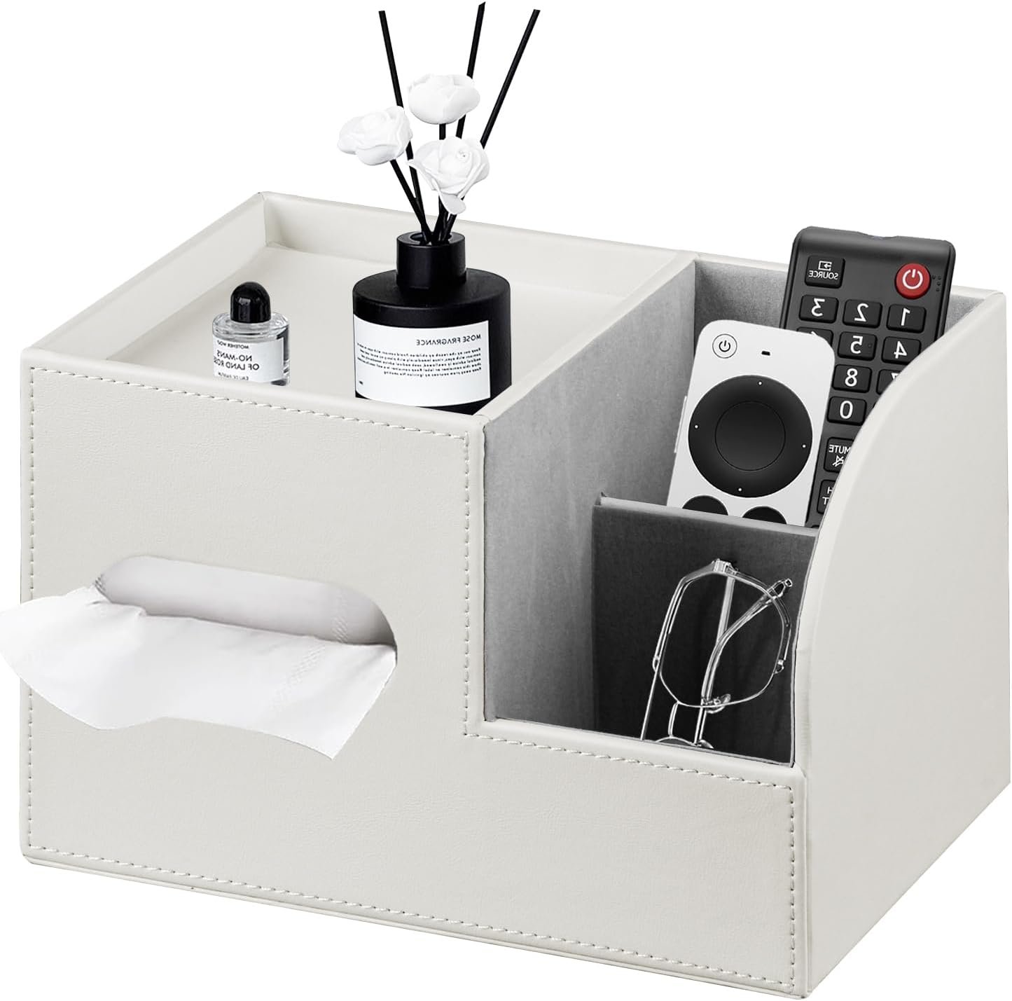 A white tissue box with tissues, a black reed diffuser with white flowers, a small bottle of essential oil, and remote controls in a compartment, along with a pair of glasses hanging from a clip.