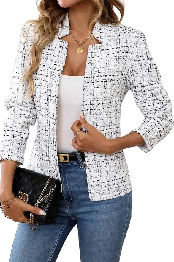A woman wearing a white textured blazer over a white top, paired with blue jeans, holding a black quilted handbag with gold chain straps, and wearing a gold necklace and rings.