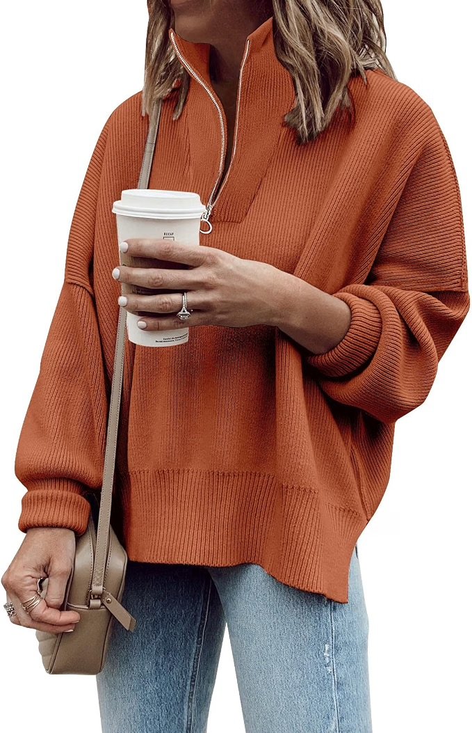 Person wearing an orange quarter zip sweater and light blue jeans, holding a disposable coffee cup and a beige purse with a strap.