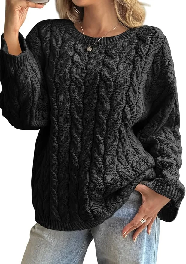 A woman wearing a chunky black cable-knit sweater, light blue jeans, and a silver necklace with a pendant.