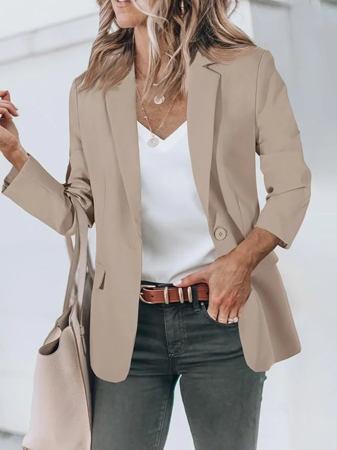 Woman wearing a beige blazer, white top, dark jeans, and a brown belt, holding a beige handbag.