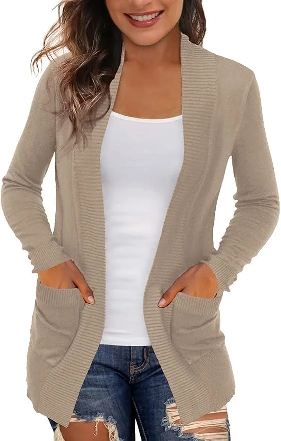 A woman wearing a beige long cardigan with pockets, a white t-shirt, and ripped blue jeans, smiling with hands in her pockets.