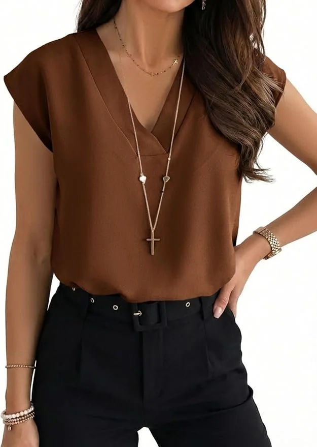 A woman wearing a brown sleeveless top, black pants with a belt, and accessorized with layered necklaces including a cross pendant, a watch, and bracelets.