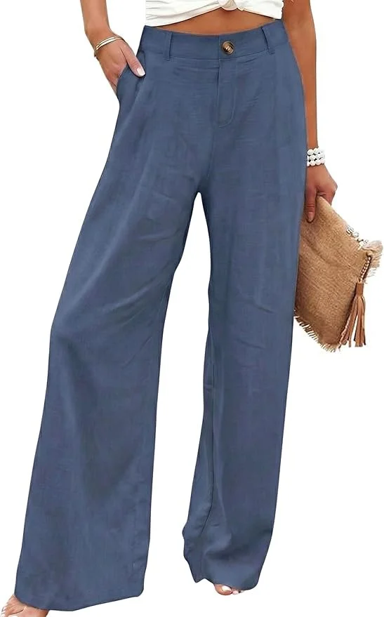 A woman is wearing loose-fitting, wide-leg blue pants with a high waist and button closure, holding a woven clutch, and wearing jewelry and a white top that is partially visible.