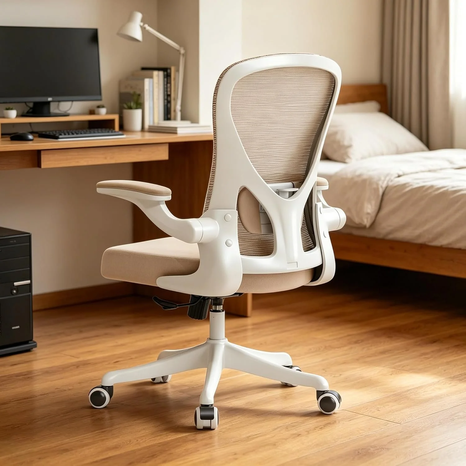 Modern ergonomic office chair with beige cushioned seat and white frame in a home bedroom with wooden floor, desk, computer monitor, and bed.