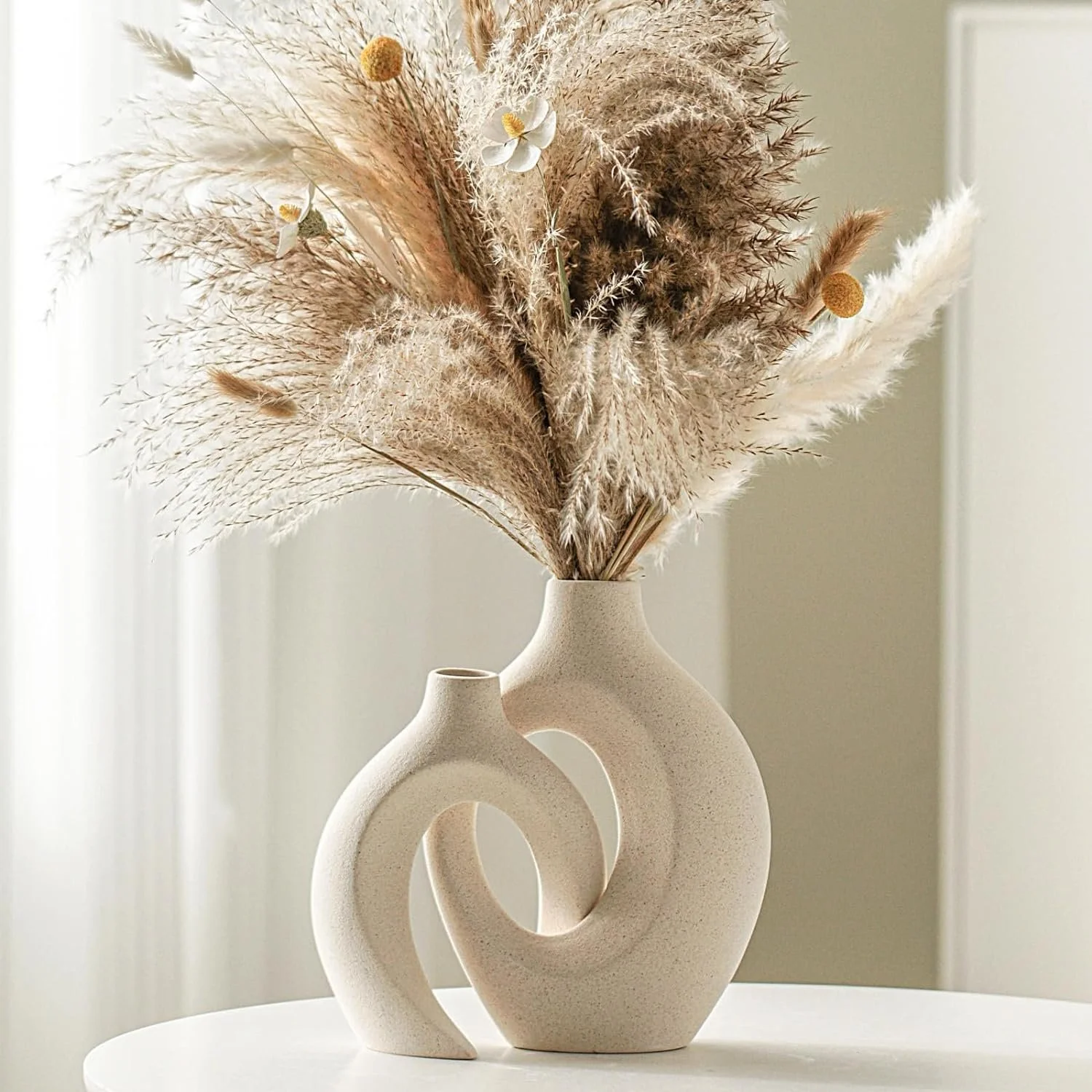 A beige ceramic vase with a circular, abstract design, holding a bouquet of dried pampas grass, flowers, and seed heads.