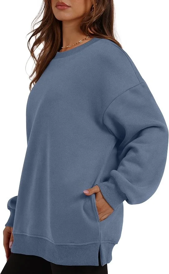 Close-up of a woman wearing a loose-fitting, long-sleeved blue sweatshirt with hand in pocket, against a white background.