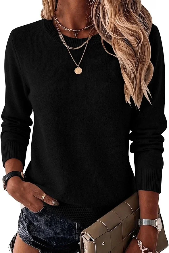 A woman wearing a black sweater, layered necklaces, a watch, and a bracelet, holding a beige handbag, with her left hand tucked into her pocket.