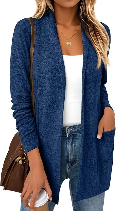 A woman wearing a dark blue coat over a white top, paired with jeans, holding a coffee cup in one hand, with a brown handbag over her shoulder, and a gold necklace.