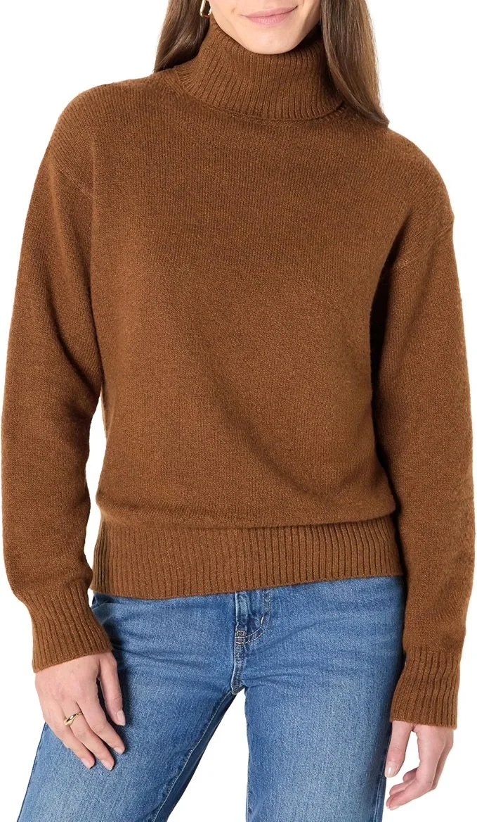 A woman wearing a brown turtleneck sweater and blue jeans.