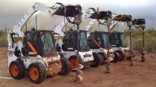 Four Bobcat S300 compact track loaders equipped with augers, lined up outdoors on dirt ground.