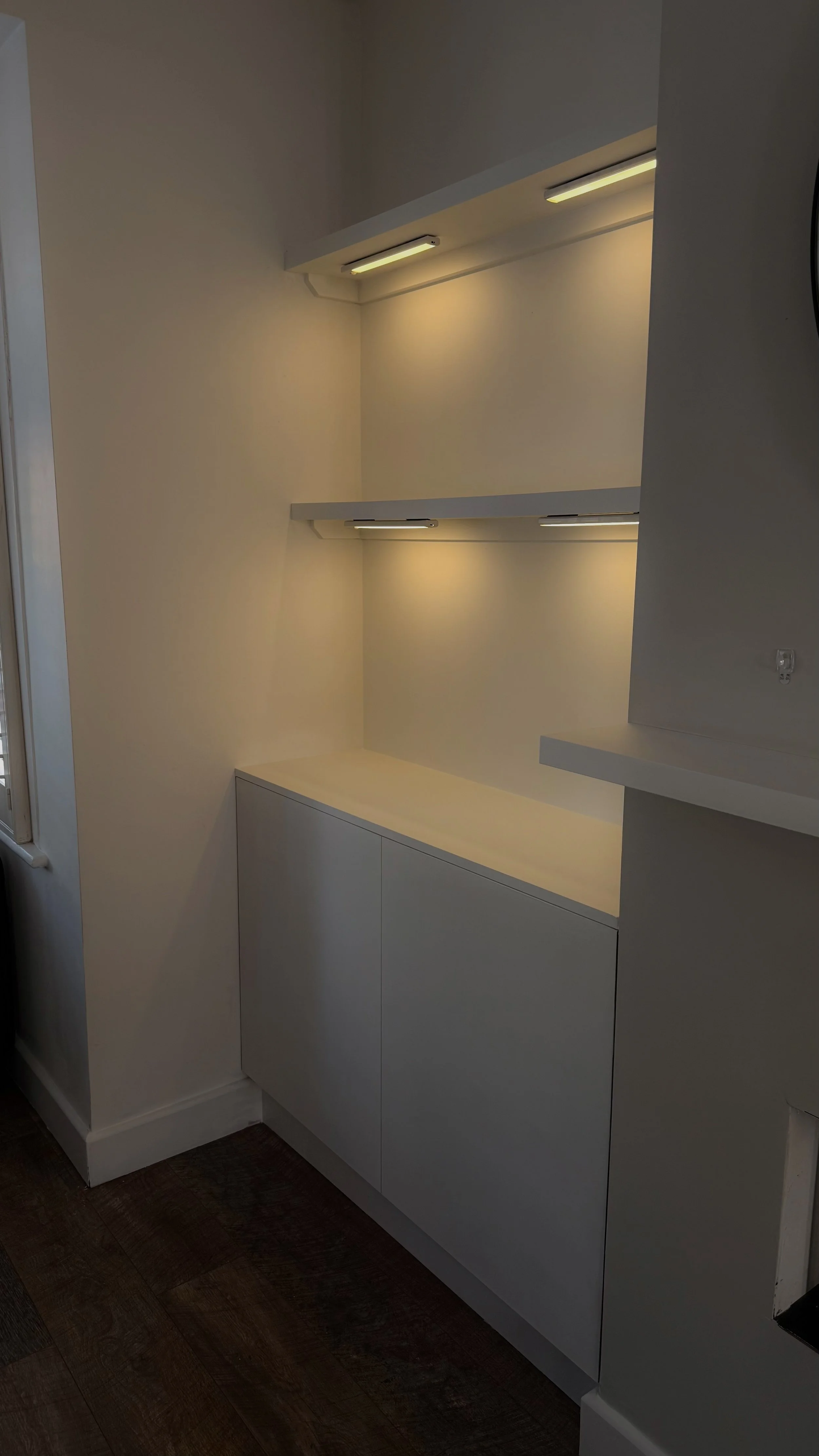 White alcove cabinet with closed doors beneath a wall-mounted shelf with built-in LED lighting.