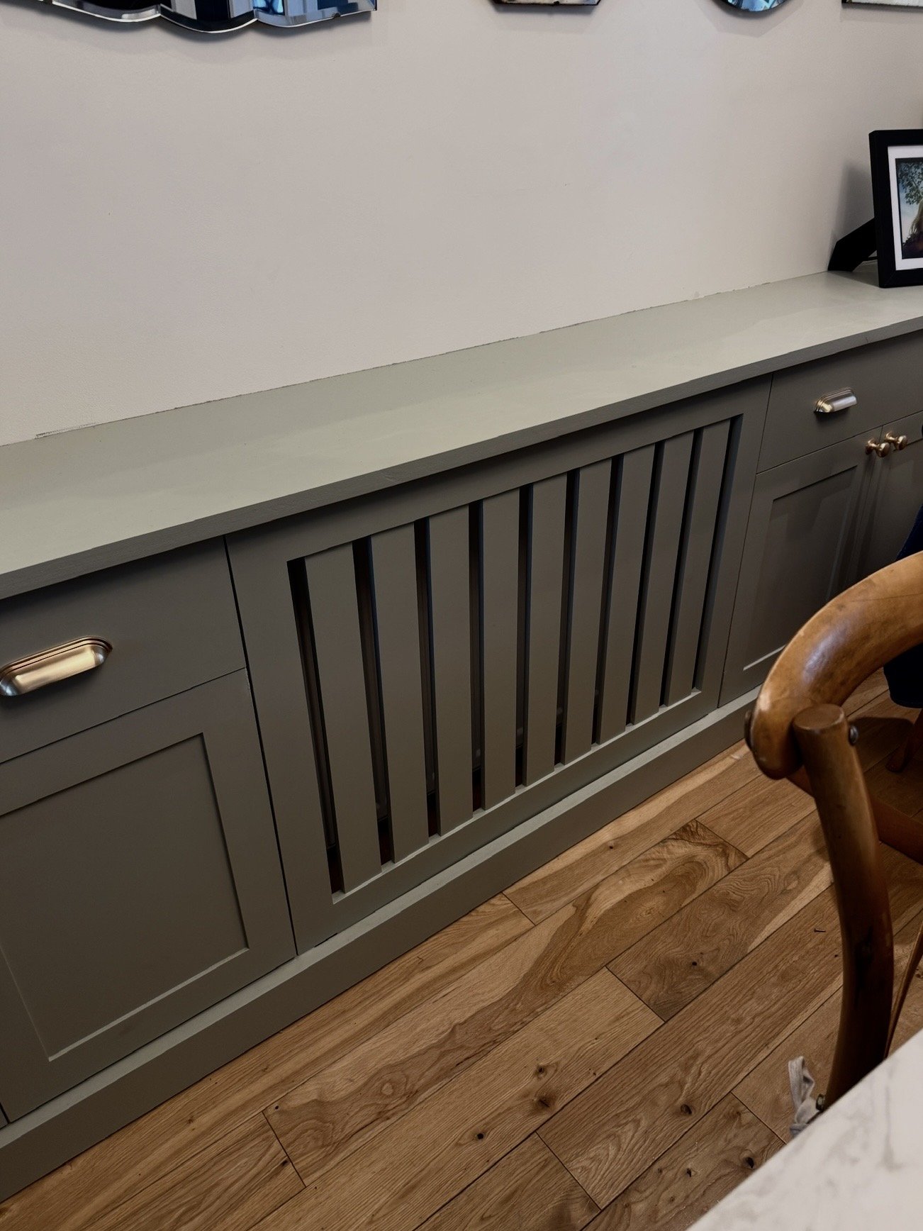 A bespoke sideboard, featuring cabinet doors and a removable radiator cover with vertical slats and brushed brass hardware.