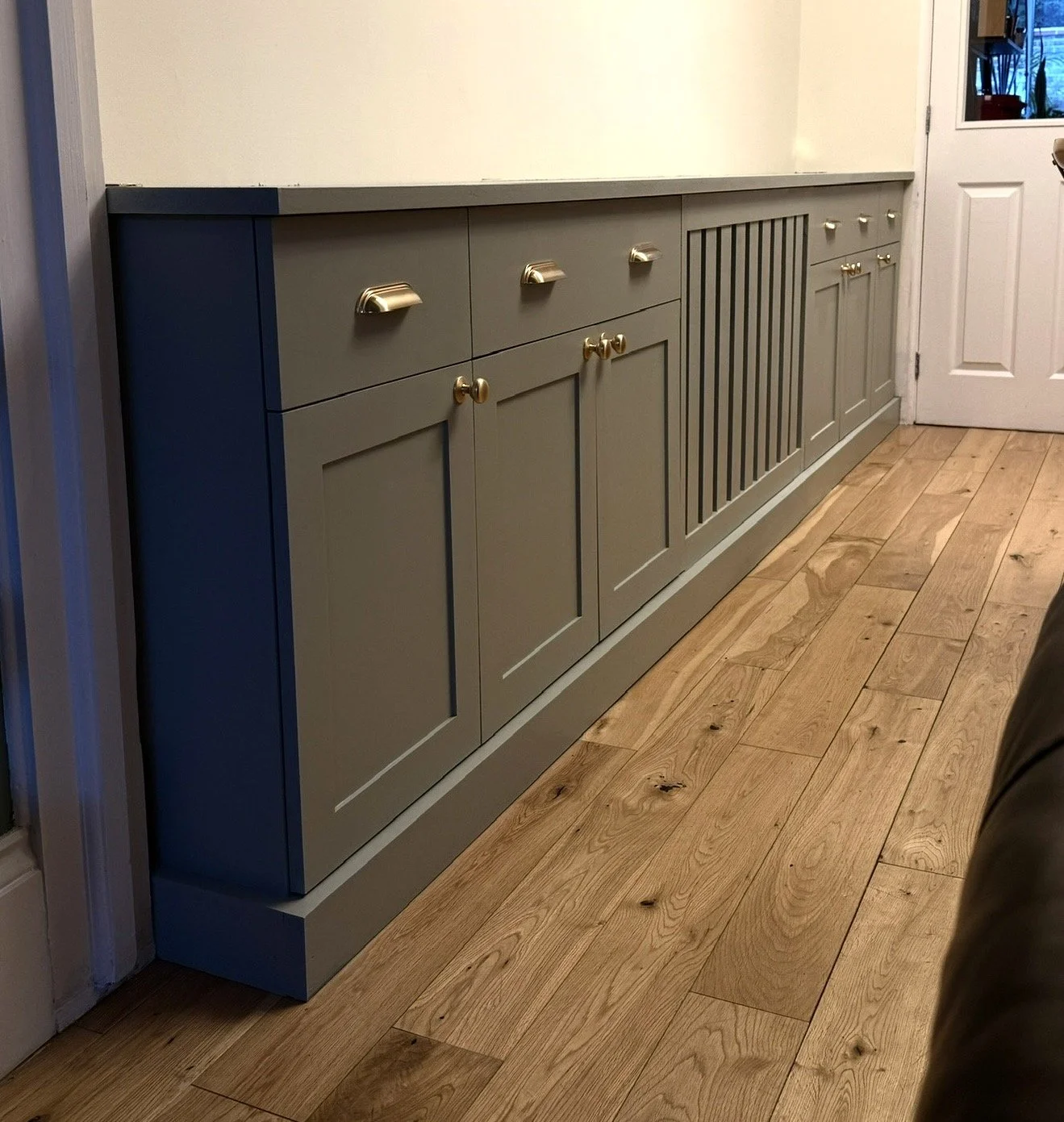 Bespoke cabinetry with brushed brass handles and brass knobs, set against a white wall and wooden floor.