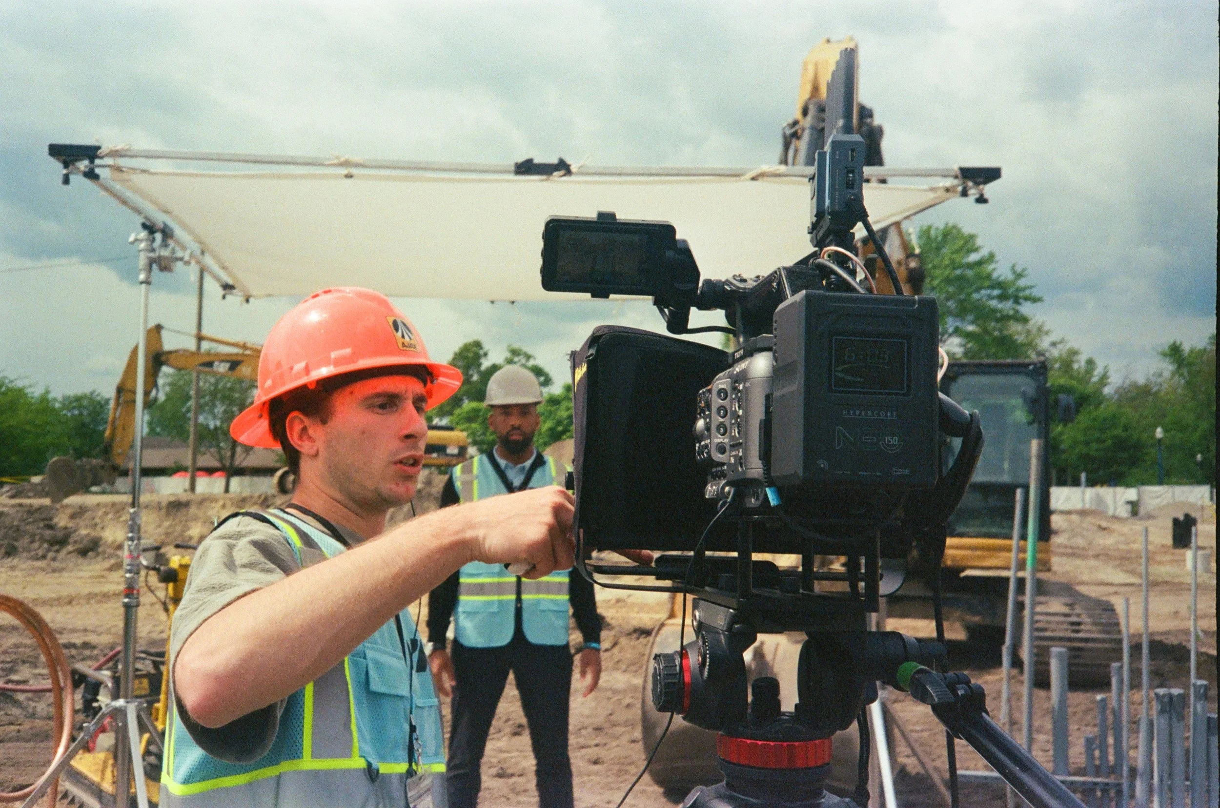 Construction workers filming with a professional camera on a construction site, wearing safety vests and hard hats
