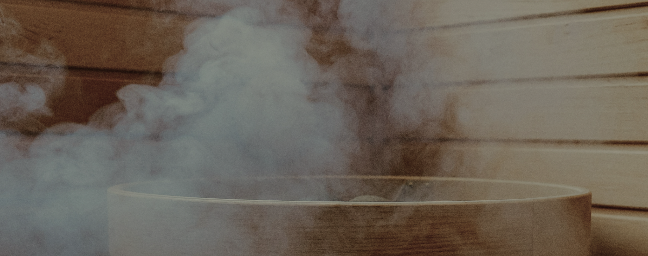 Steam rising from a wooden bowl or container, set against a wooden wall background.