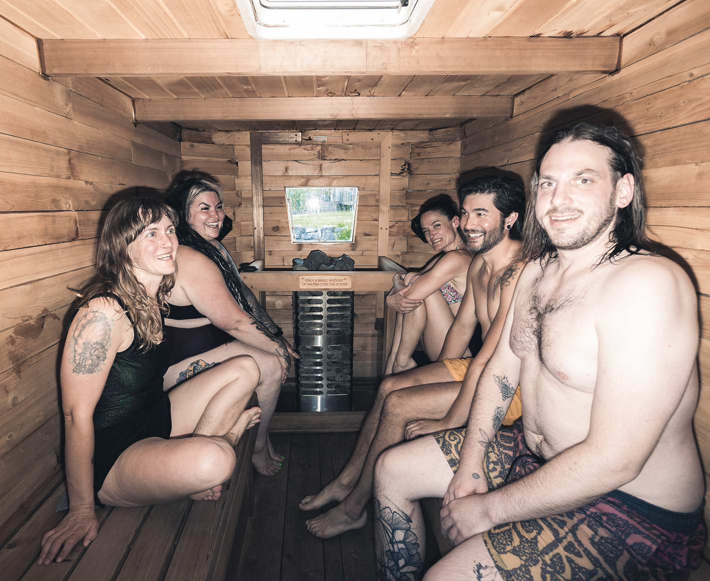 Group of people enjoying a sauna together in a wooden room, smiling and sitting on benches.