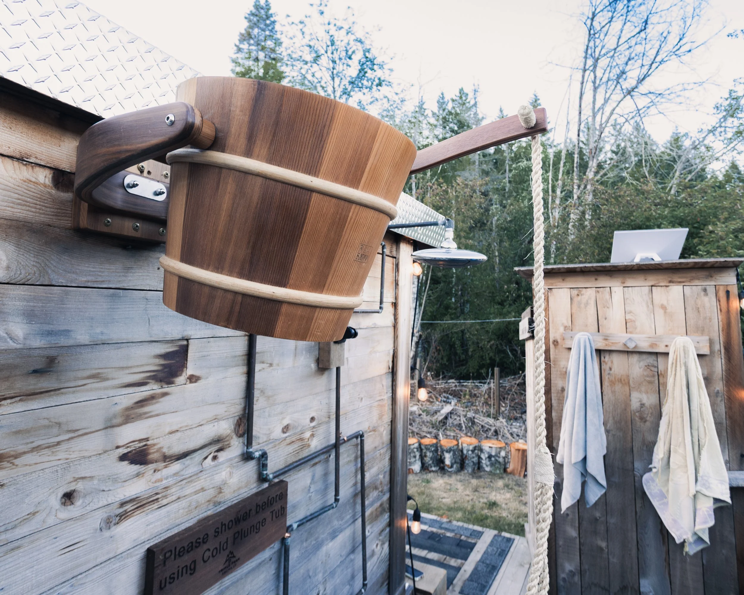 Close-up of a wooden shower bench with a white towel hanging on a rope, outdoors with trees in the background.