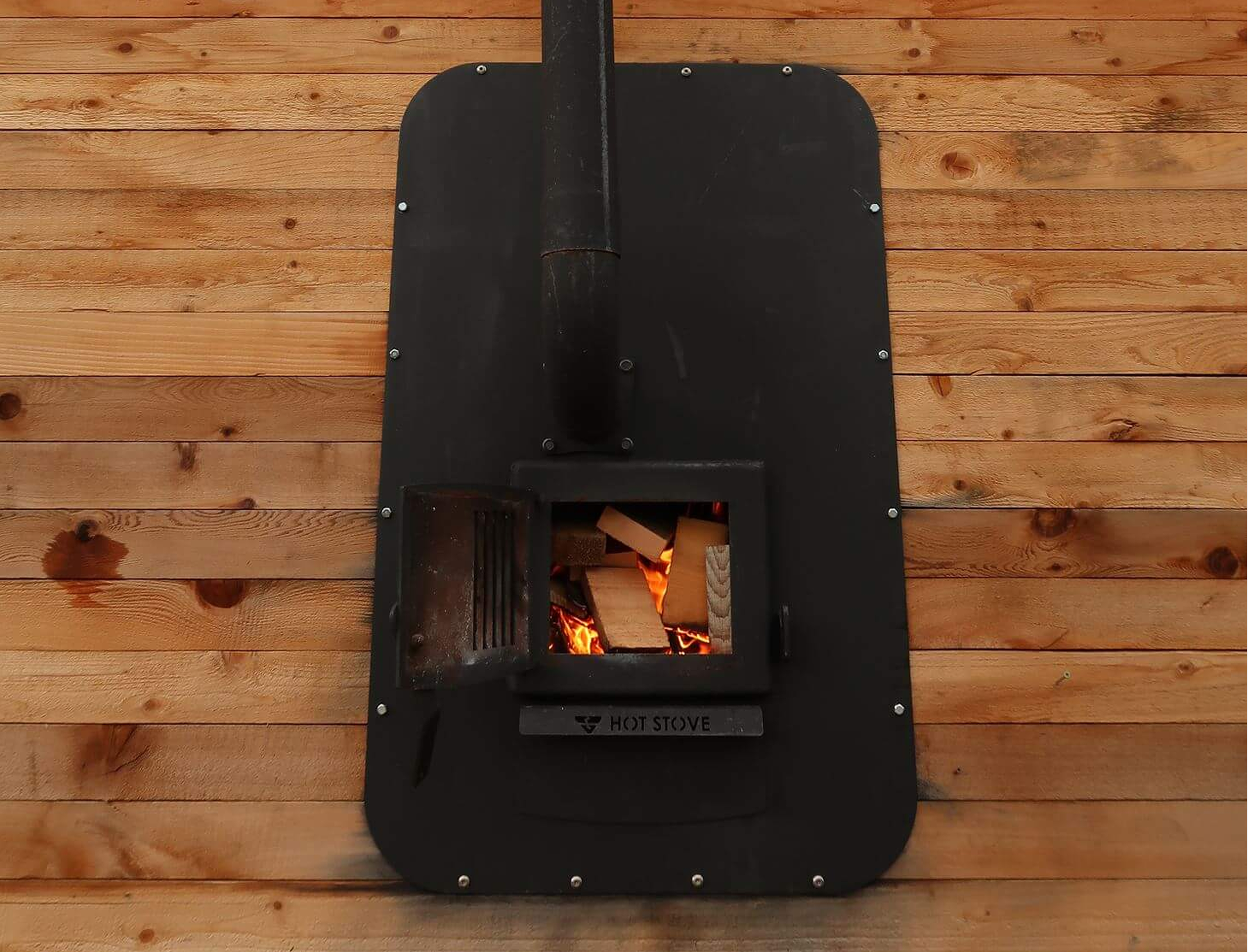 A black wood stove with flames visible inside, placed on a wooden floor.