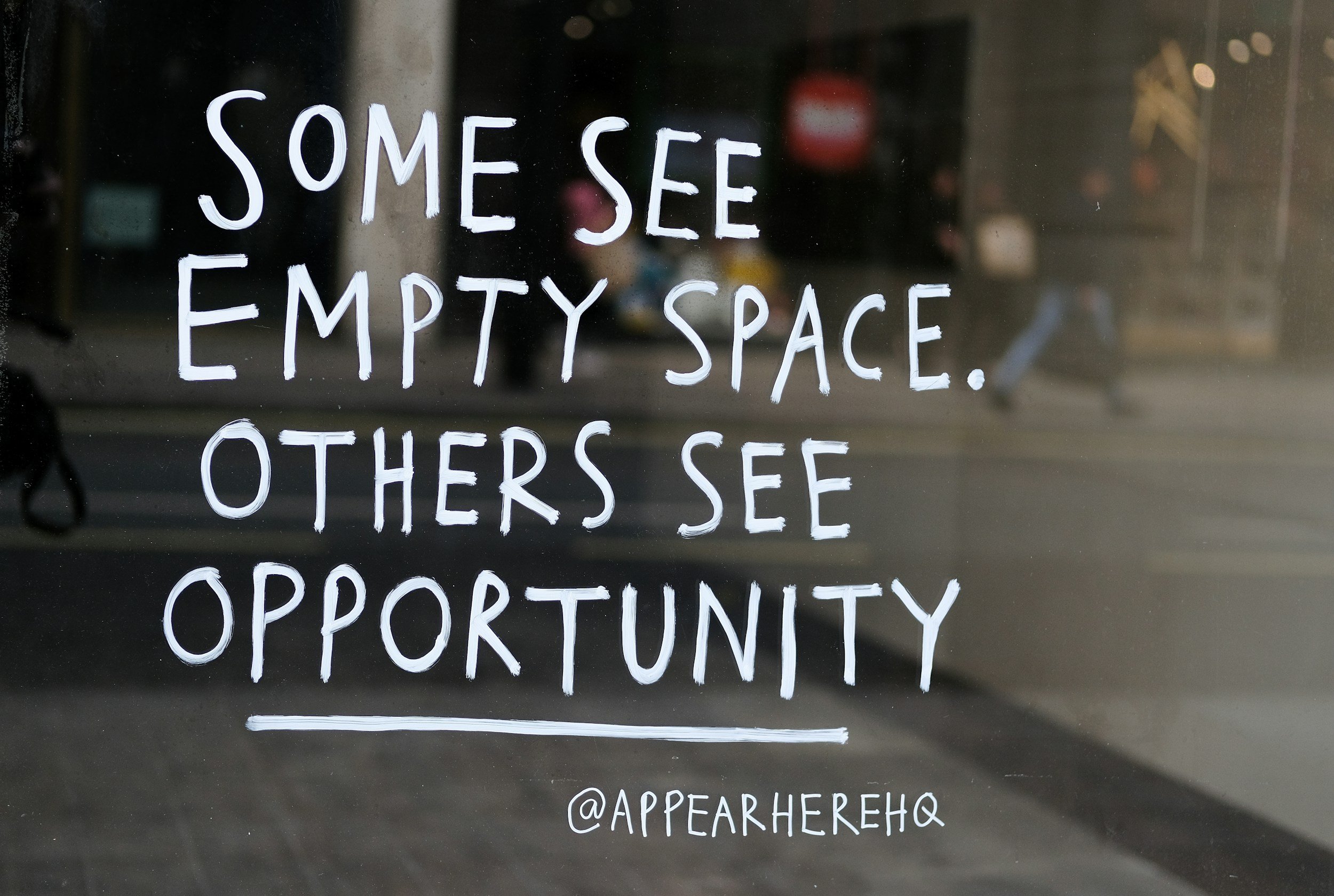 Handwritten sign on glass window that reads, "Some see empty space. Others see opportunity," with the Instagram handle '@appearherehq' at the bottom.