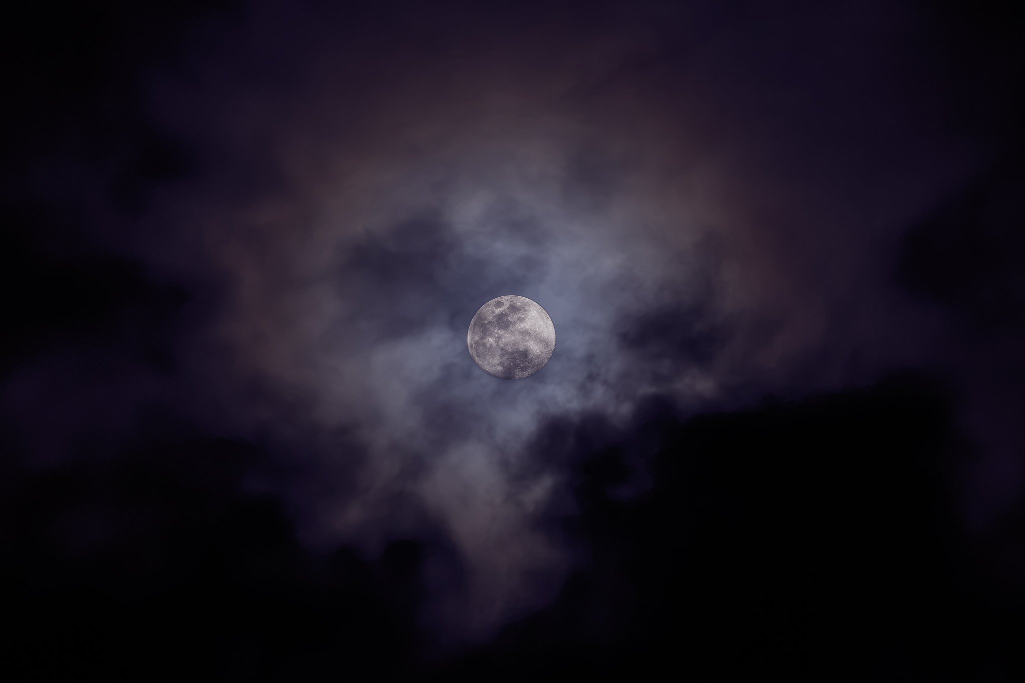 The moon emerging through a veil of dark purple clouds.