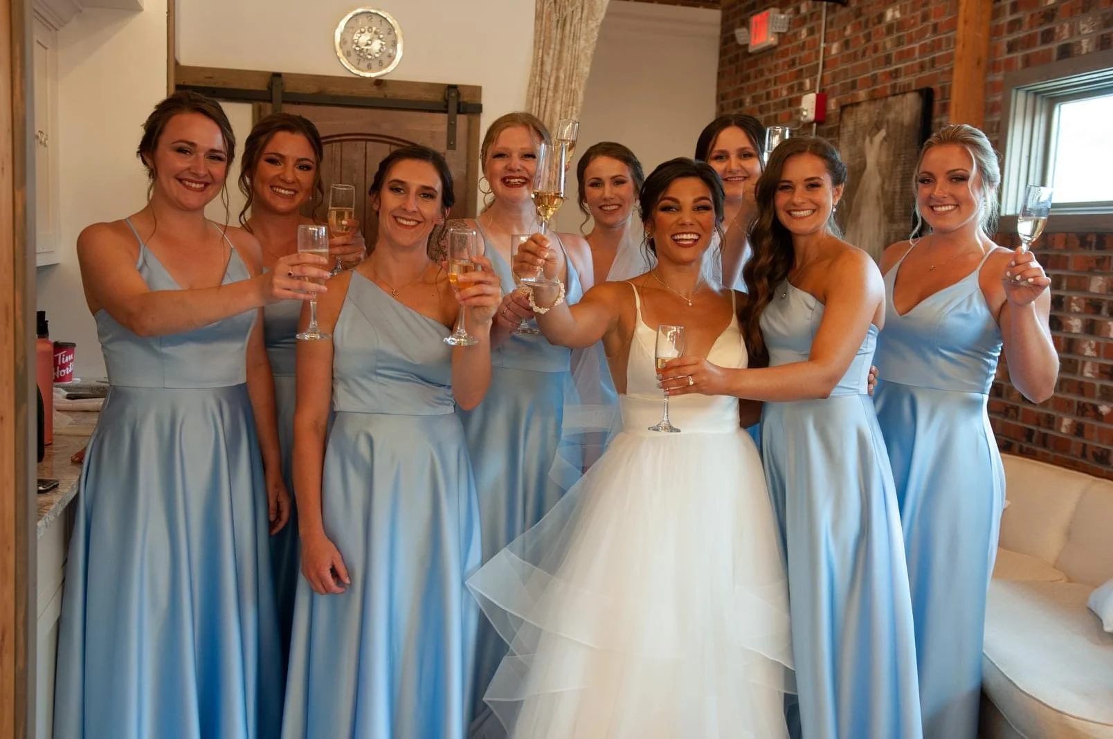 A group of women at a wedding, with the bride wearing a white dress and the bridesmaids in matching light blue dresses, holding champagne glasses and smiling.