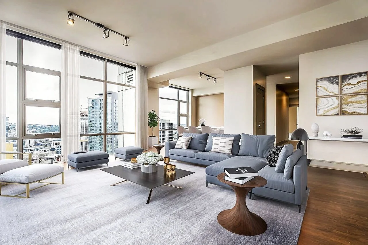 Modern living room with large windows, gray sofa, coffee table, accent chairs, and decorative items.