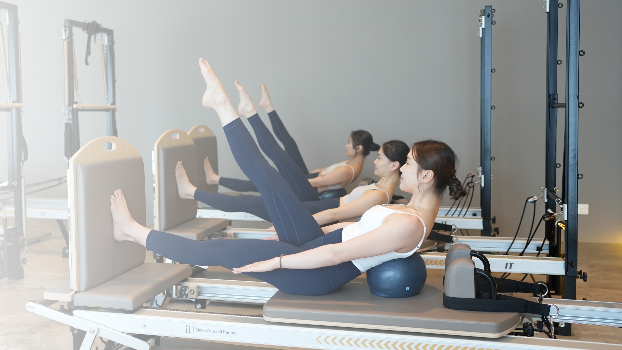 Four women in workout attire participating in a Pilates class on specialized reformer beds in a fitness studio.