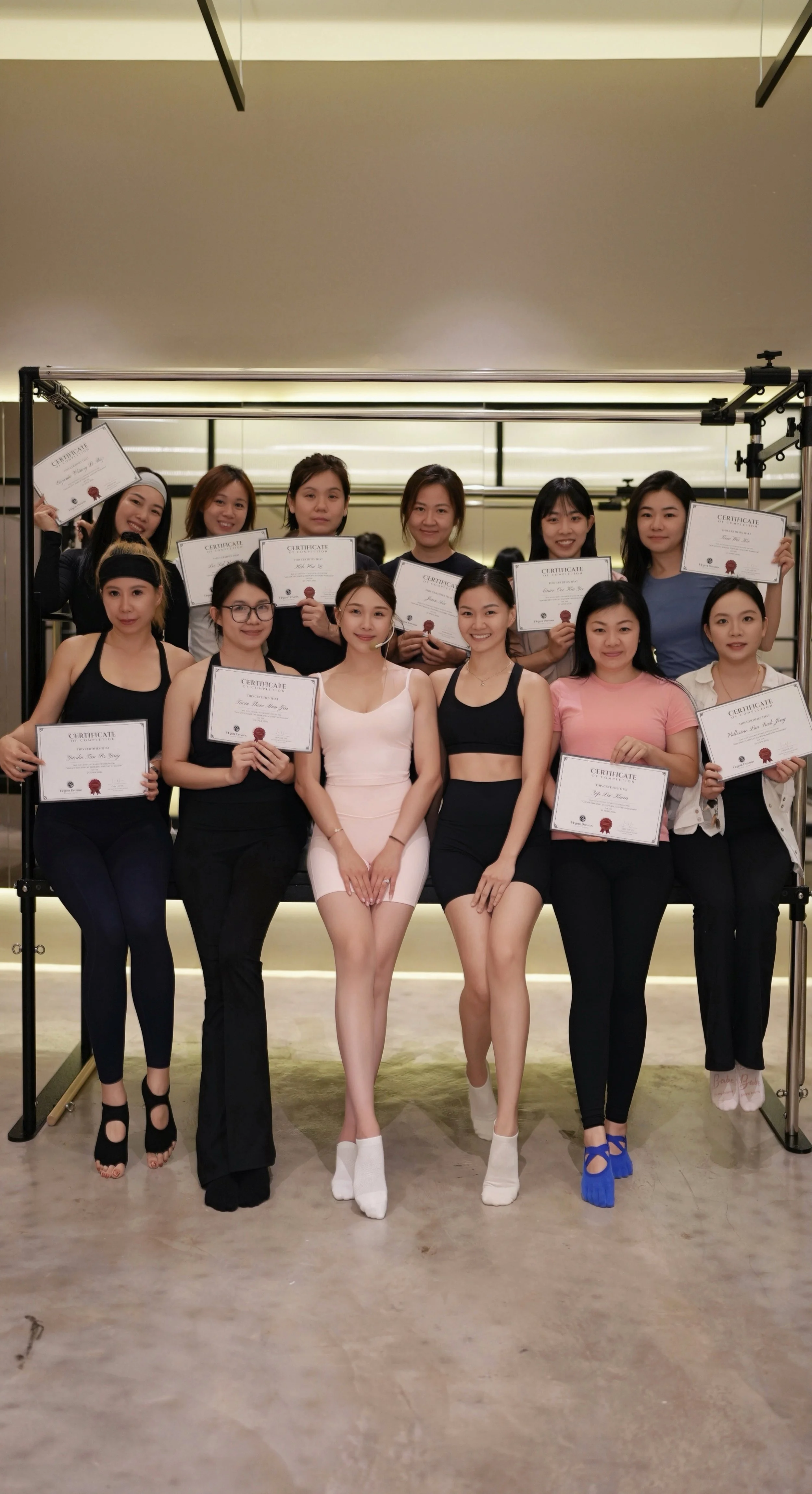 Group of women holding certificates, posing indoors, with some women kneeling in the front row and others standing behind.