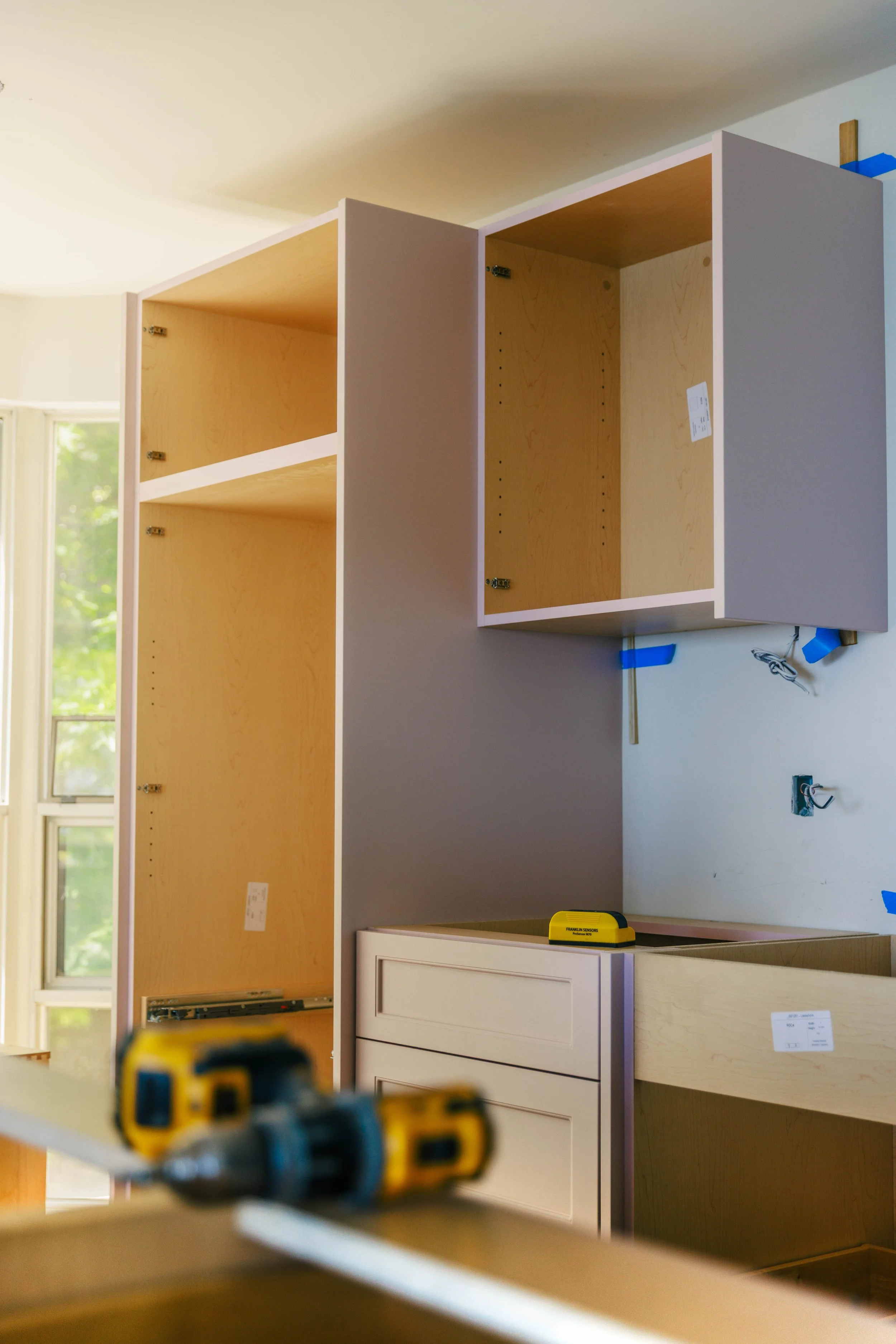Unassembled wooden cabinets in a room under construction or renovation, with tools and construction materials nearby.