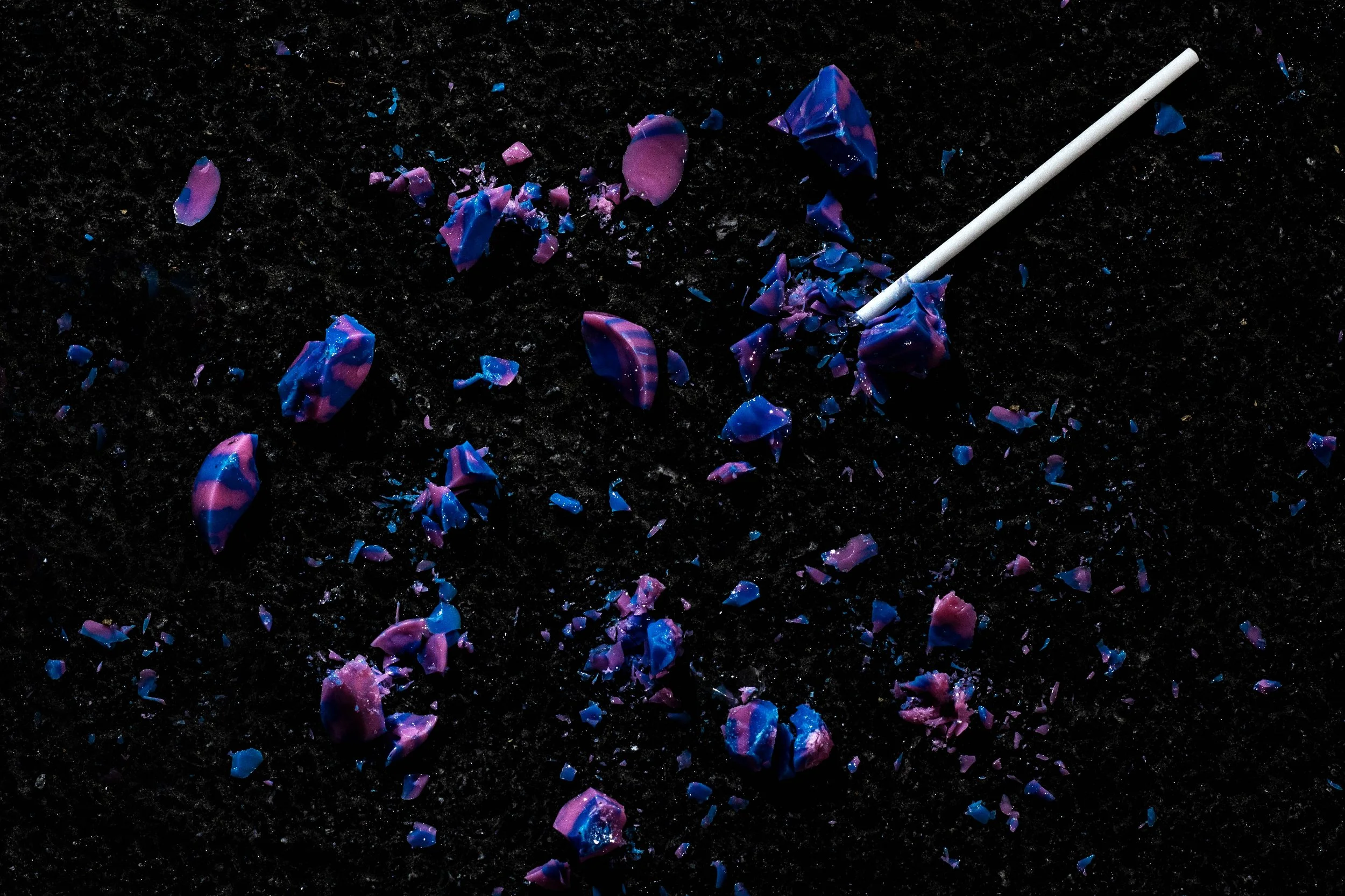 Broken pieces of colorful plastic or resin with a swab stick on a dark surface.