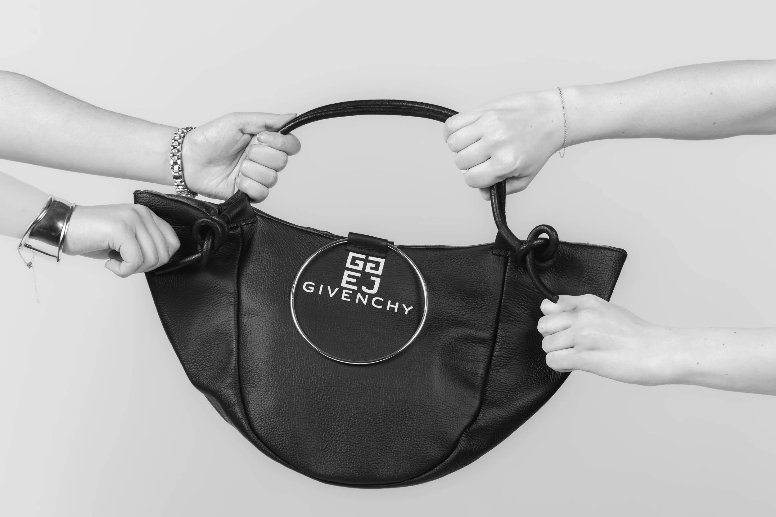 Two hands pulling on a black designer handbag with a circular logo tag that reads 'GIVENCHY' against a plain background.