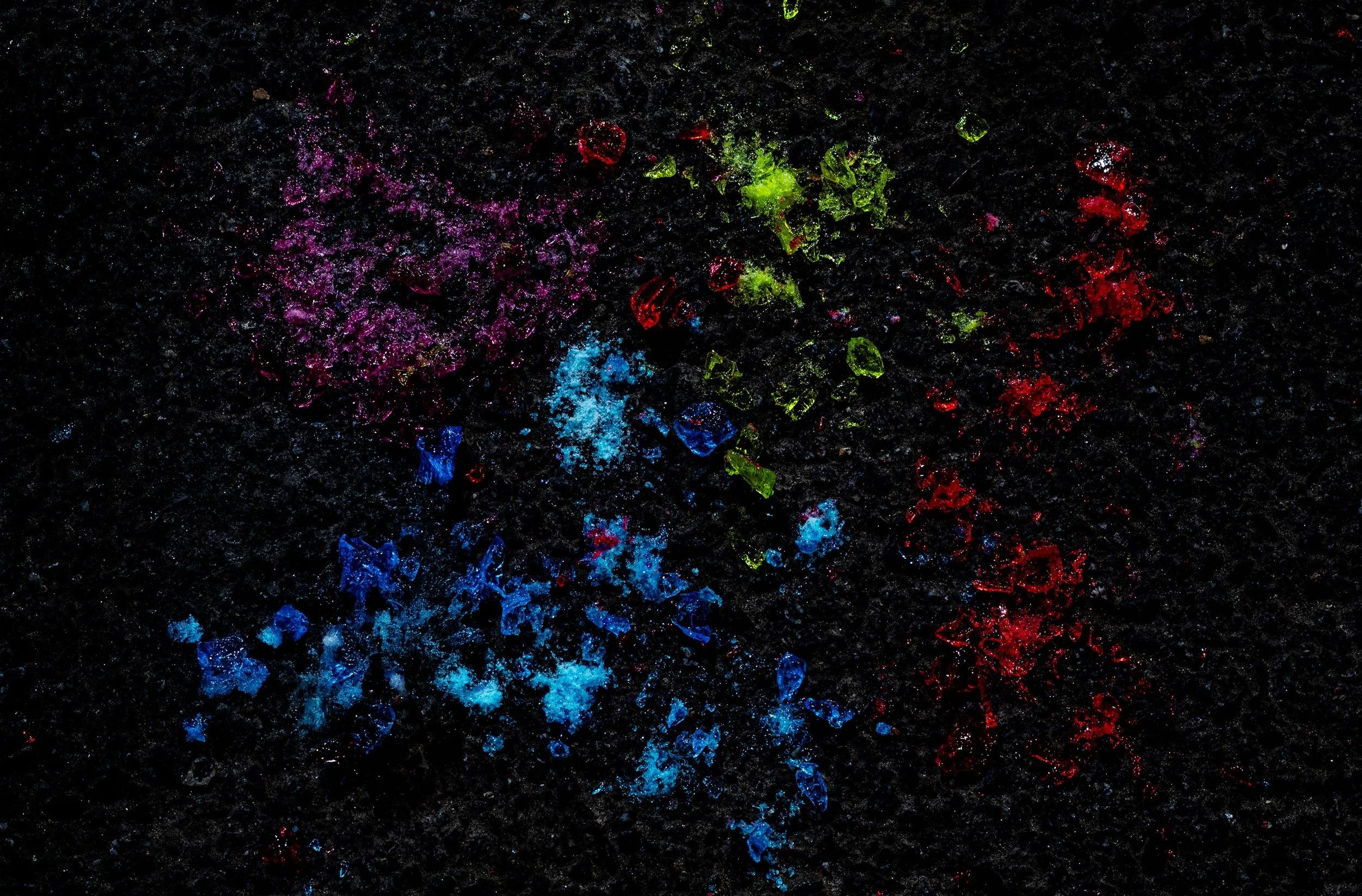 Colorful glitter scattered on a black background, featuring hues of purple, pink, red, green, blue, and white.