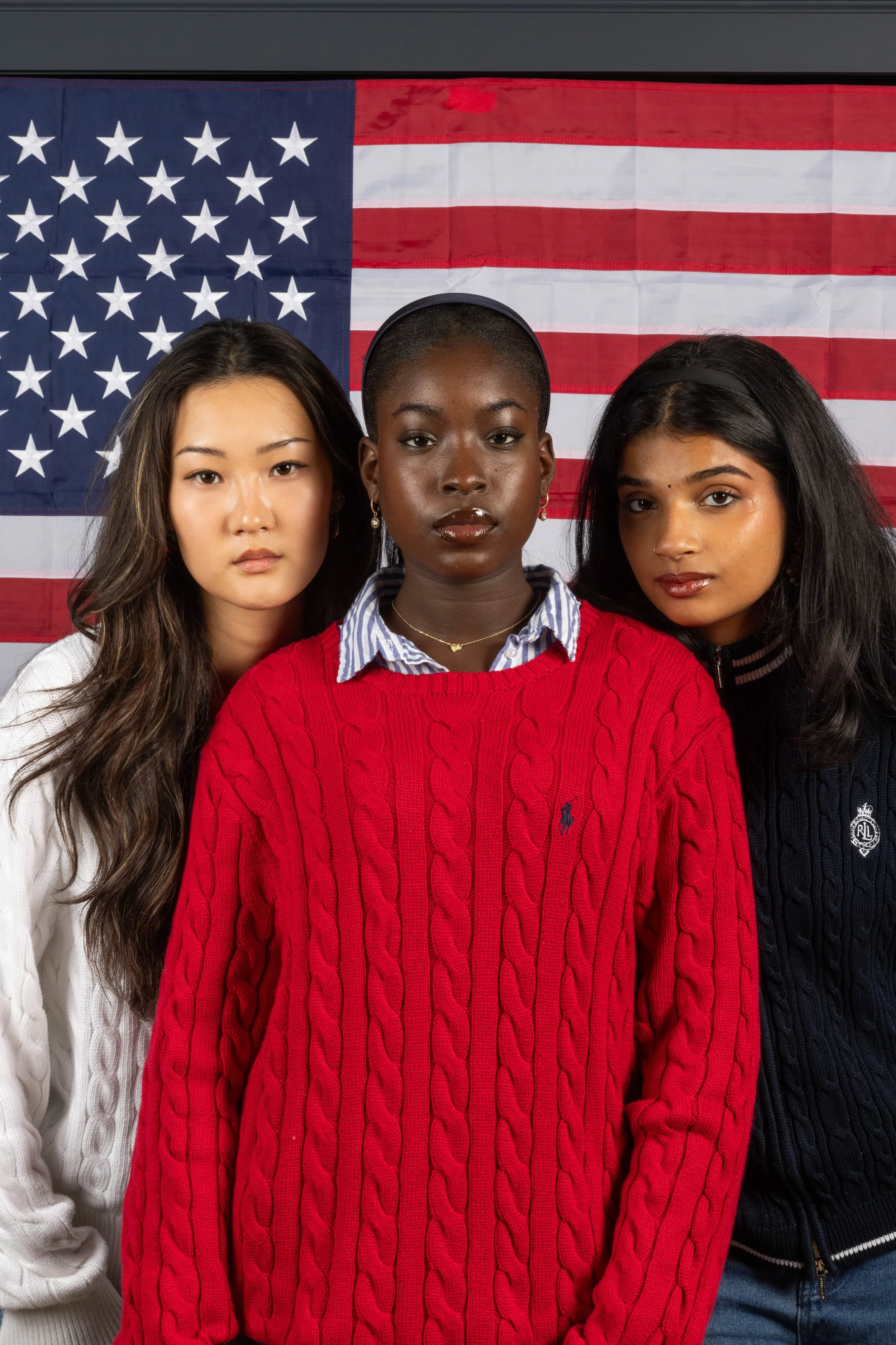 Three women standing side by side in front of an American flag.
