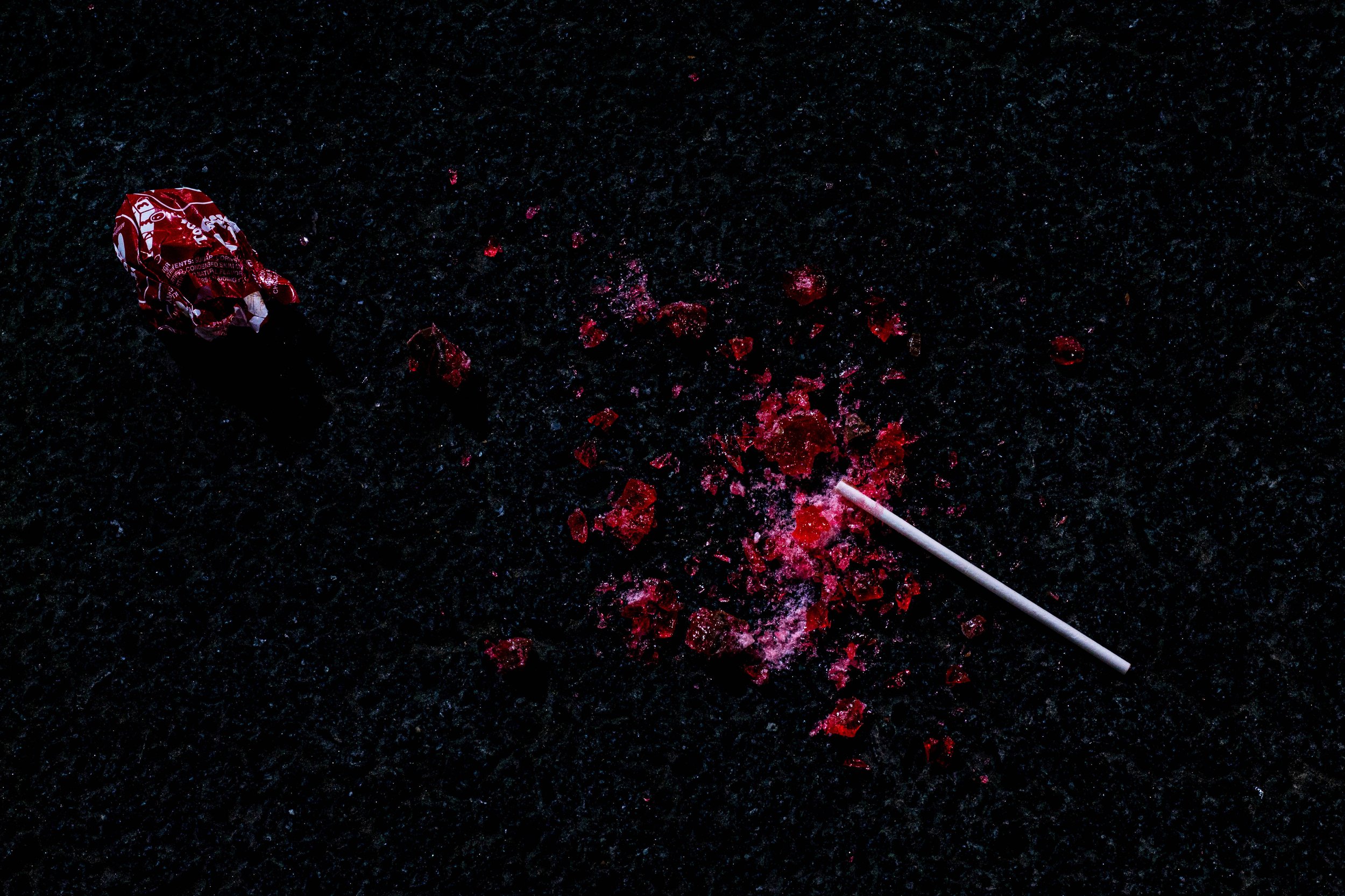 A crumpled red and white can and red spilled confetti on a dark surface with a white straw nearby.