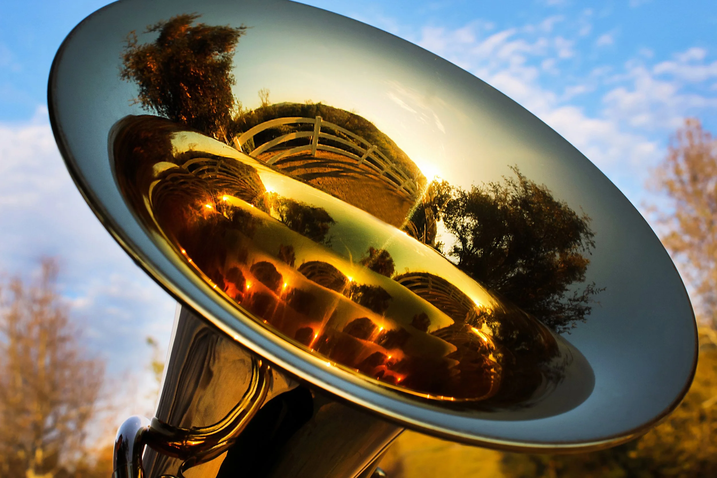 Close-up of a motorcycle mirror reflecting a bridge, trees, and a sunset sky.