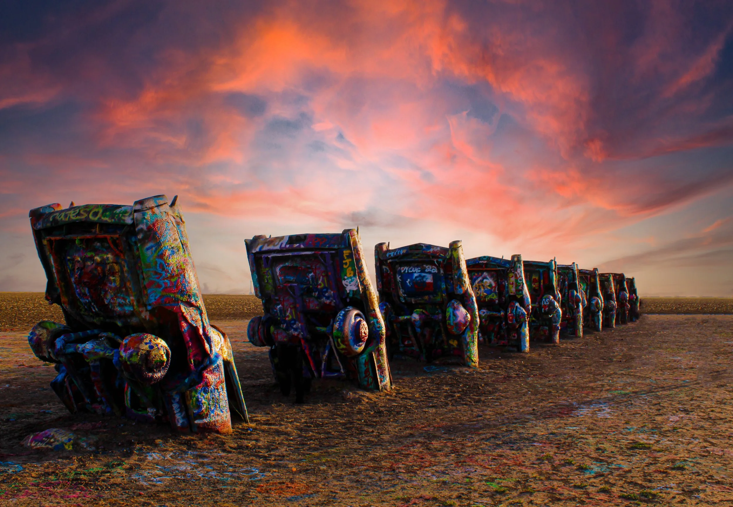 Colorfully painted and graffiti-covered chairs lined up on a beach at sunset with a colorful sky.