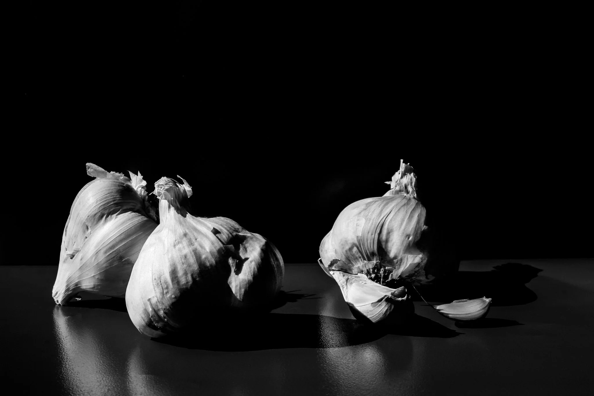 Black and white photo of garlic heads and separated garlic cloves on a reflective surface.