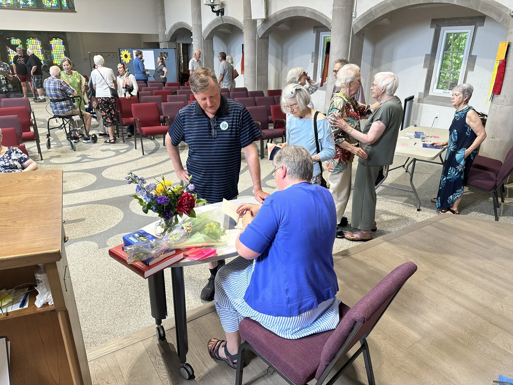 Elisabeth Jones signing books at the Book Launch at Cedar Park. Other people are chatting while in line for their books to be signed.
