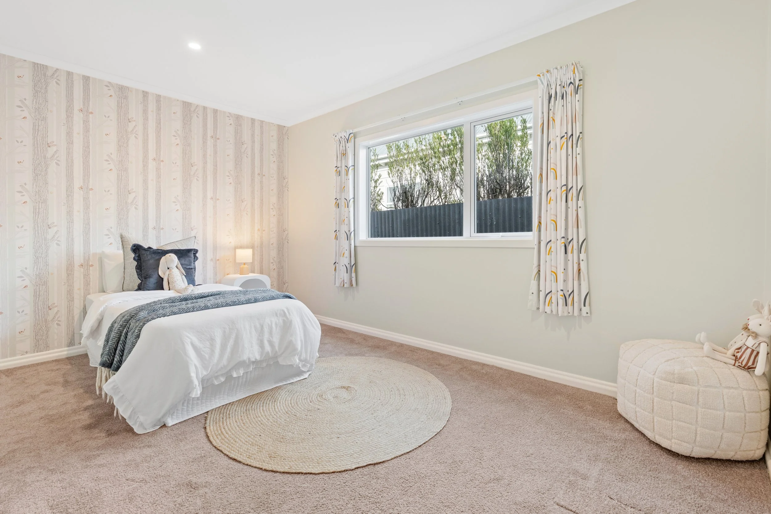 A bedroom with a bed, curtains, window, and a plush bunny on the bed.