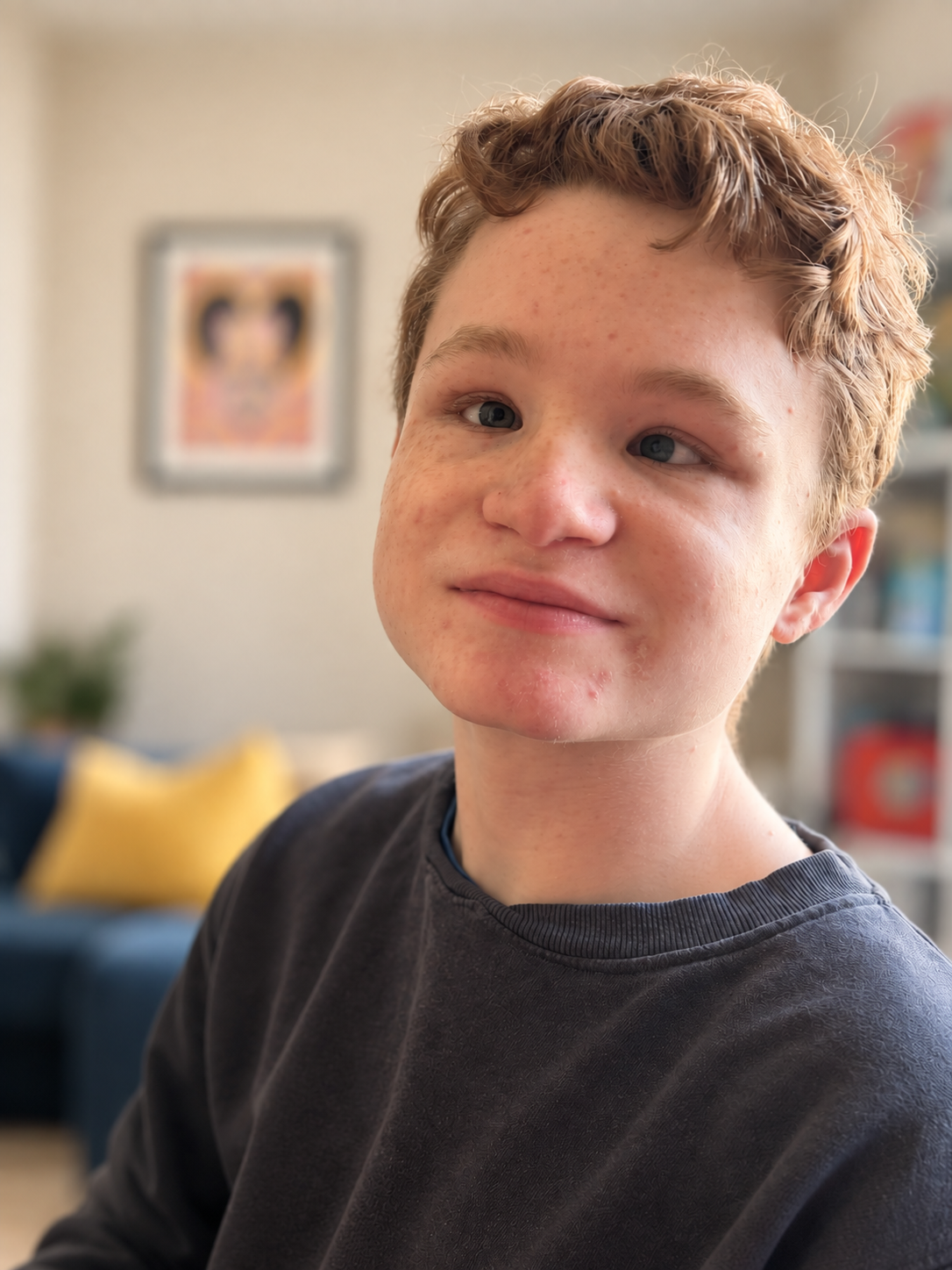 Close-up of a young boy with red hair and freckles, wearing a black shirt in a cozy living room.