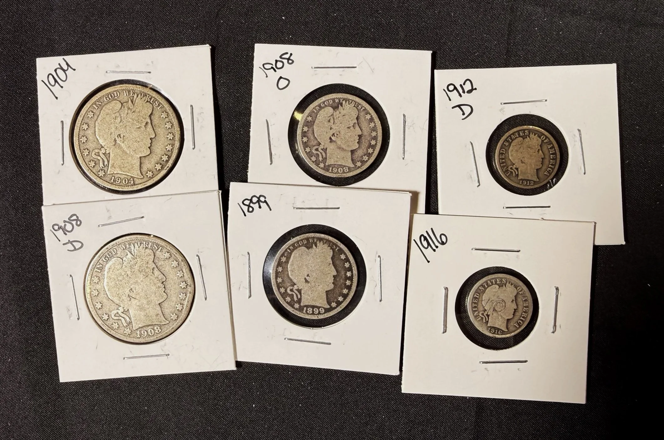Photograph of three antique US coins in white coin holders, labeled with years 1904, 1908, and 1912, on a black surface.