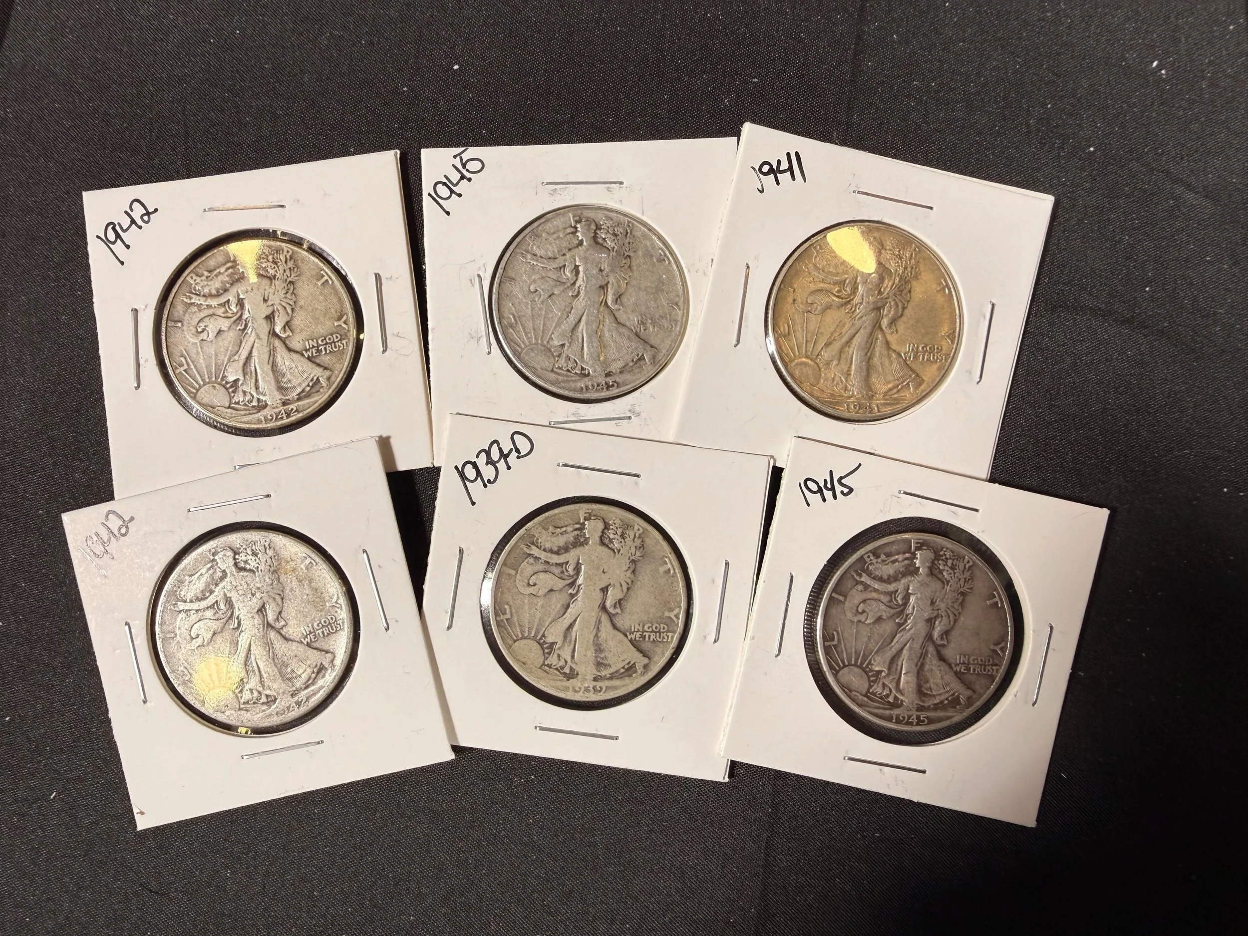 Six coins in protective holders with handwritten labels indicating years 1942, 1945, and 1941, placed on a dark fabric surface.