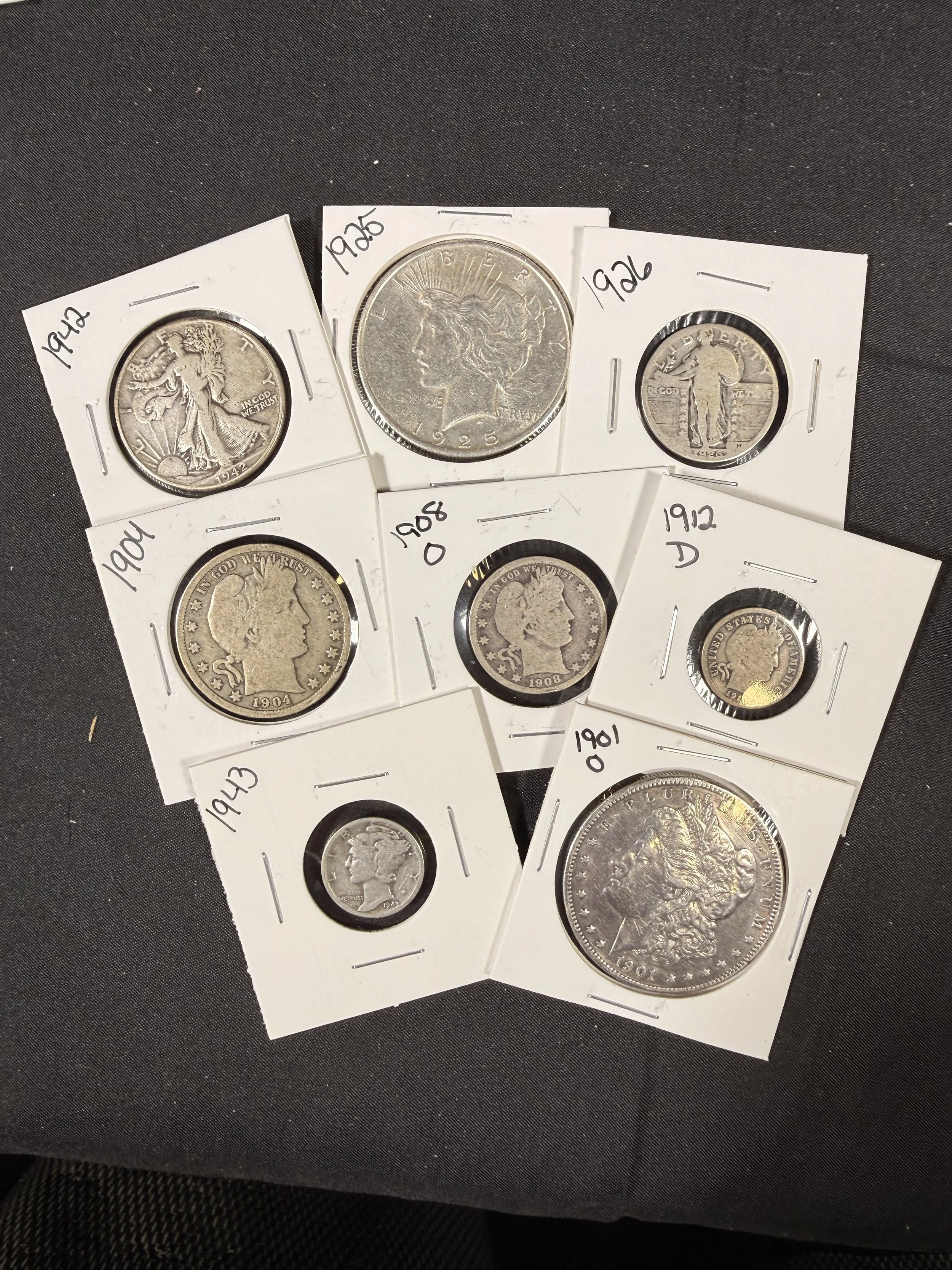 Collection of five silver coins in cardboard holders with handwritten year labels, including 1942, 1926, 1904, 1908, and 1912, arranged on a black surface.