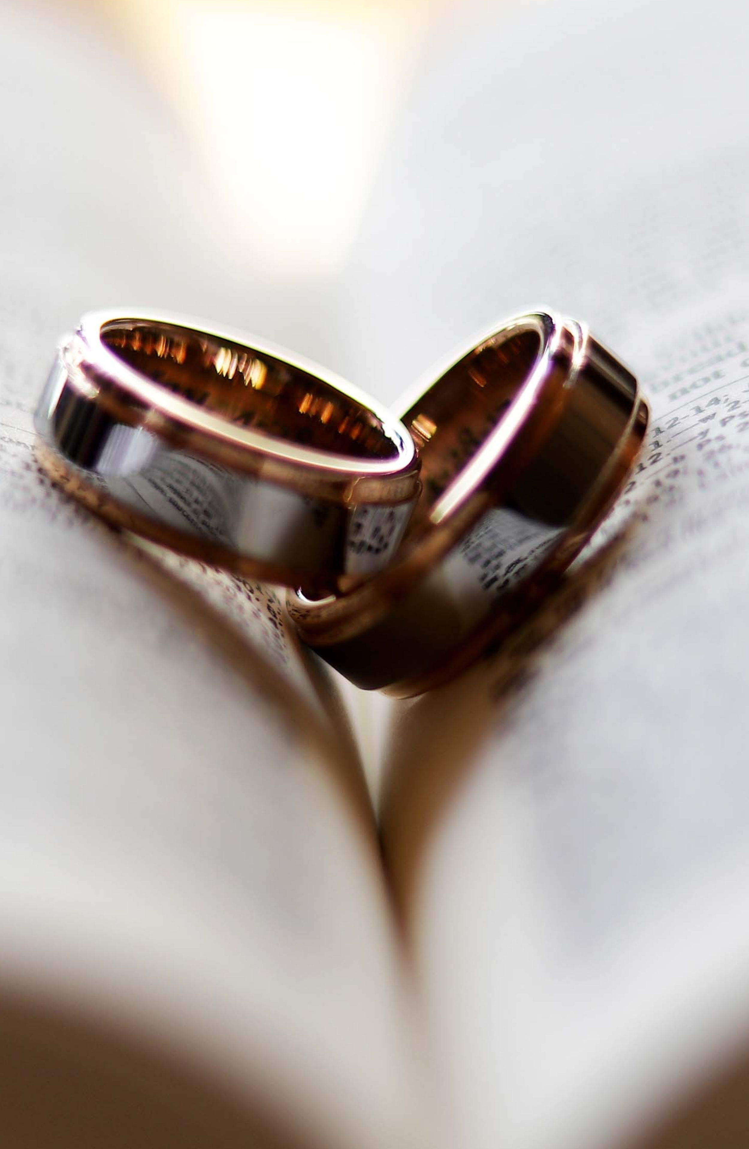 Close-up of two stacked wedding rings on an open book or pages, casting a shadow.