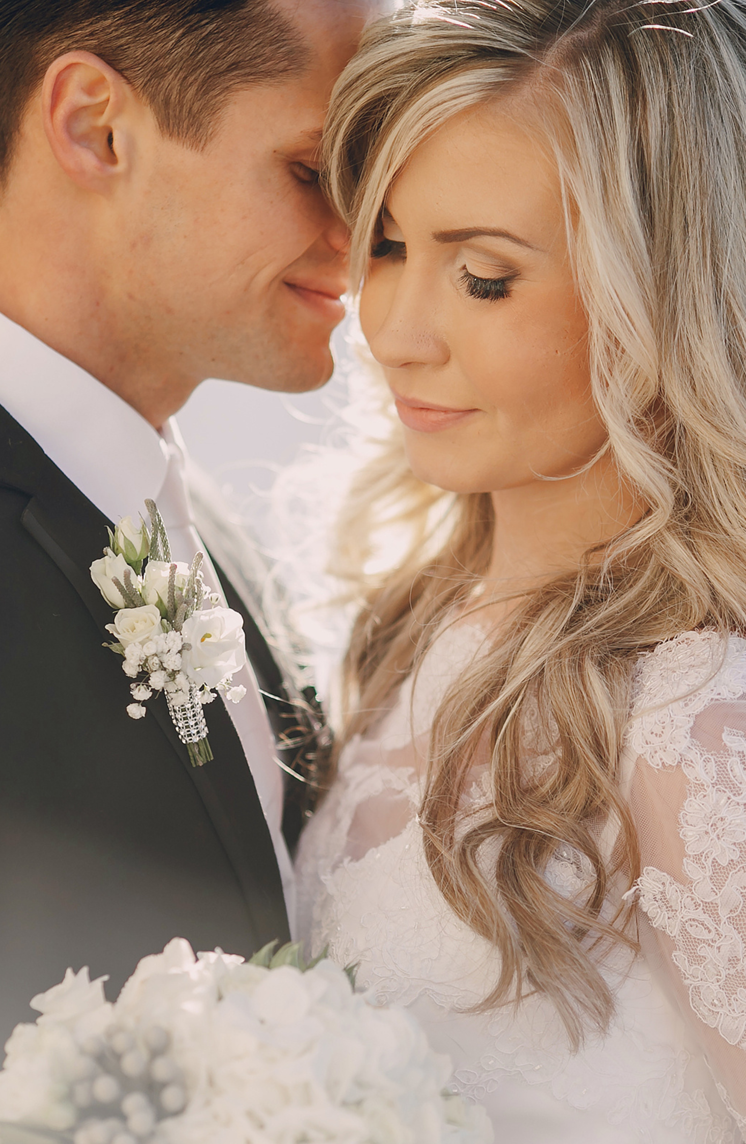 A bride and groom close together with foreheads touching, eyes closed, smiling gently during their wedding.