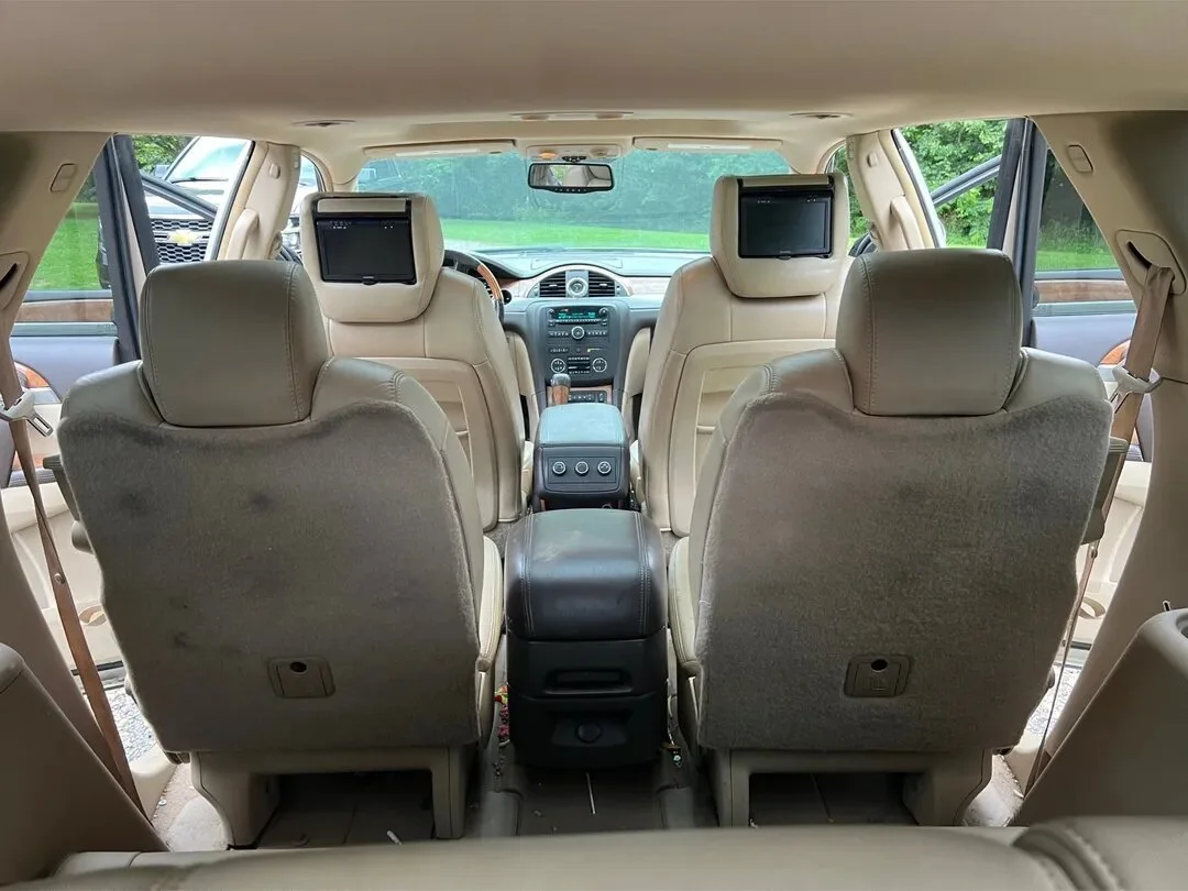 The interior of a beige SUV showing three rows of seats, with the back two rows having headrest monitors, and the front row visible through the windshield.